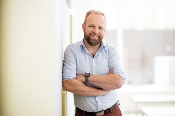 A man with a beard, his arms crossed, smiling at the camera