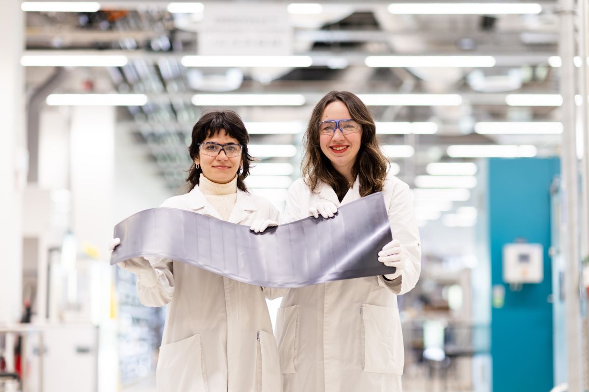 2  women in lab coats holding solar cells, smiling at the camera.