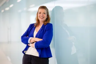 A woman in a blue blazer, arms crossed, smiling at the camera