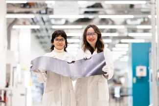 2  women in lab coats holding solar cells, smiling at the camera.