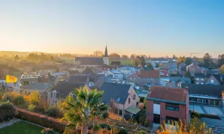 Panoramisch stadsgezicht bij zonsondergang met een prominente kerktoren.