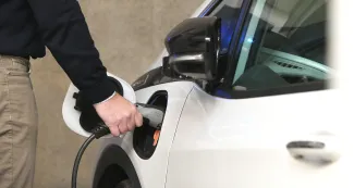 Een man sluit de lader van een elektrische auto aan.