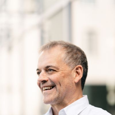 A man in a white shirt smiling, looking away from the camera