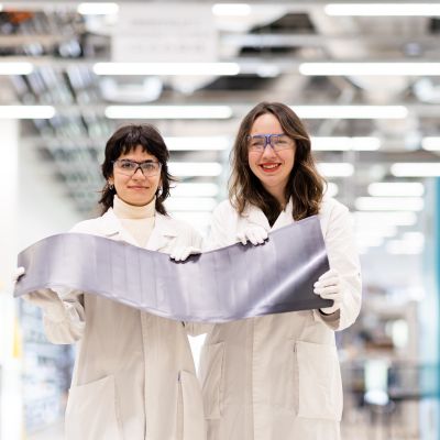 2  women in lab coats holding solar cells, smiling at the camera.
